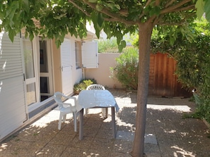 A patio with a table and chairs, a tree, and a building with shutters.