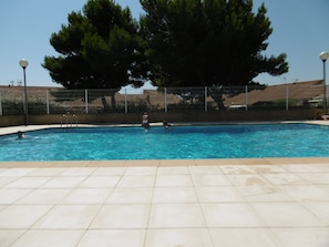 Una piscina con un borde de baldosas, escaleras metálicas y una valla.