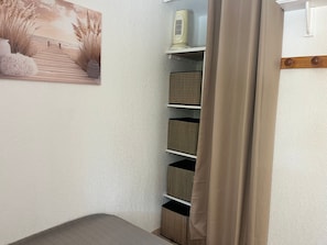 Esquina de una habitación con un estante que contiene cestas, un purificador de aire de pared y un cuadro enmarcado.