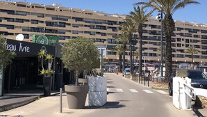 A hotel with a modern design, featuring a large building with multiple floors and balconies. There is a sign for 'Teau Ivre' on the left side of the image. Palm trees line the street in front of the hotel. - Charming 3-Room Villa with Mezzanine, Steps from Beach and Port in Saint-Cyprien (Saint-Cyprien)