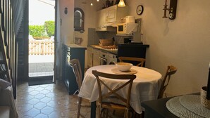A compact kitchen with a dining area, featuring a wooden table, chairs, and a small island with a microwave. - Charming 3-Room Villa with Mezzanine, Steps from Beach and Port in Saint-Cyprien (Saint-Cyprien)