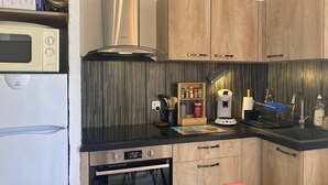 Eine kompakte Küche mit Mikrowelle, Backofen und integrierter Dunstabzugshaube. Es ist ein Holzschrank mit einer Gewürzregal und einer Kaffeemaschine vorhanden.