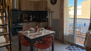 Ein Essbereich mit einem Tisch für vier Personen, umgeben von roten Stühlen, sowie eine Küche mit Holzschränken und einer Uhr an der Wand.