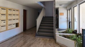 Un couloir avec un escalier, des boîtes aux lettres et une personne au fond.