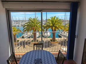 Een balkon met een tafel en stoelen, met uitzicht op een jachthaven met boten en palmbomen.