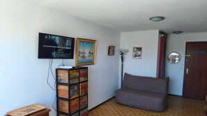 Un salon comprenant un canapé, un téléviseur fixé au mur, un meuble avec des tiroirs et un tapis à motifs.