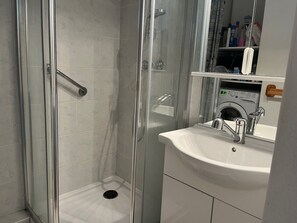 Une salle de bain moderne avec une douche à parois de verre, un lavabo blanc et un lave-linge encastré.