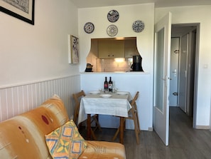 A compact living space with a dining area, a sofa with patterned cushions, and a kitchen visible through an archway.