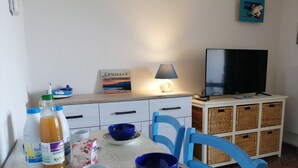 A dining area with a table set for two, a television, and a bookshelf.