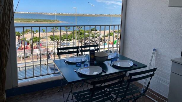 A balcony with a table set for two, overlooking a beach and a bridge.