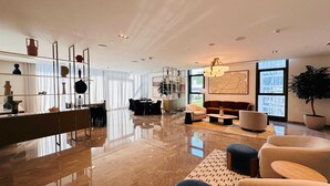 A modern living room with a large window, a dining area, and a kitchen with a glass partition.