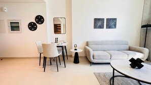 A modern living room with a grey sofa, a round coffee table, and a dining area with a white table and chairs. There are decorative plates on the wall and a small round table with a decorative item.