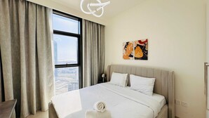 A hotel room with a large bed, a view of the cityscape through a window, and a modern light fixture.