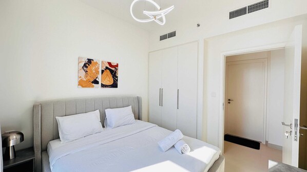 A modern bedroom with a large bed, white bedding, two artwork pieces on the wall, and a wardrobe with sliding doors.