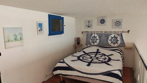 A bedroom with a bed, a window with a blue frame, and nautical-themed decor. - Cosy T2 Mezzanine, Terrasse, Parking Privé, Proche Plage et Village, Idéal Famille, Animaux Ok (Gruissan)