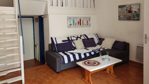 A cozy living room with a sofa, a coffee table, and a painting on the wall. - Cosy T2 Mezzanine, Terrasse, Parking Privé, Proche Plage et Village, Idéal Famille, Animaux Ok (Gruissan)