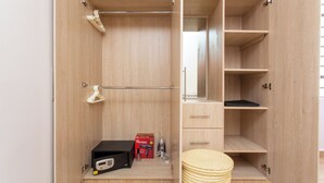 Un armario de madera con varios estantes y cajones, una barra para colgar ropa y una mesita con una caja y un secador de pelo.