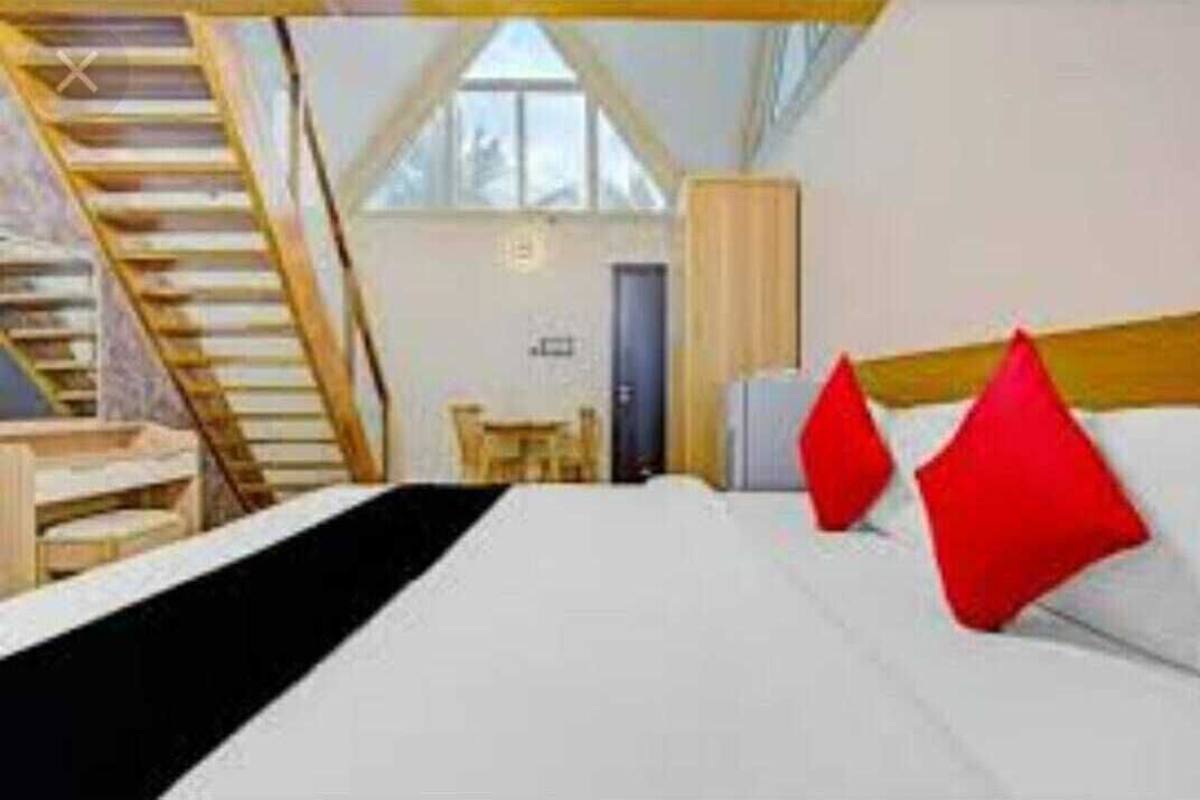 A bedroom with a bed, red pillows, a wooden headboard, a staircase, and a window.