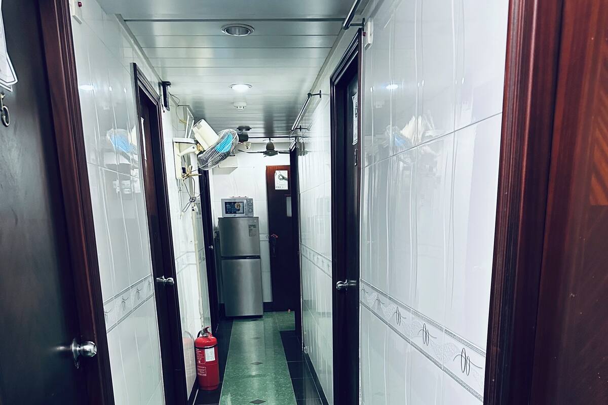 Un pasillo con paredes y piso de baldosas verdes que conduce a una habitación con refrigerador y extintor.