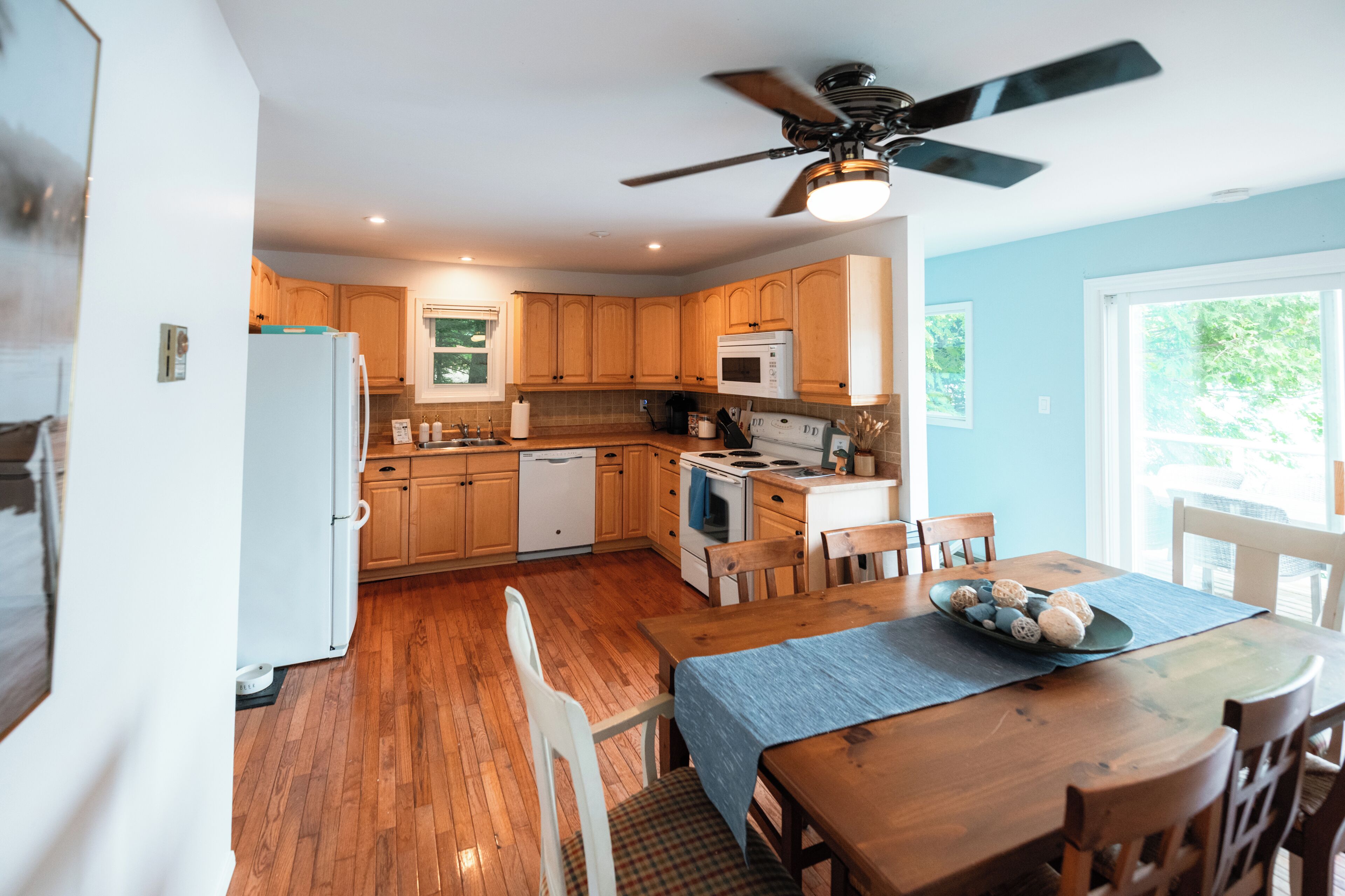 A kitchen with wooden cabinets, a white refrigerator, a stove, and a ceiling fan.