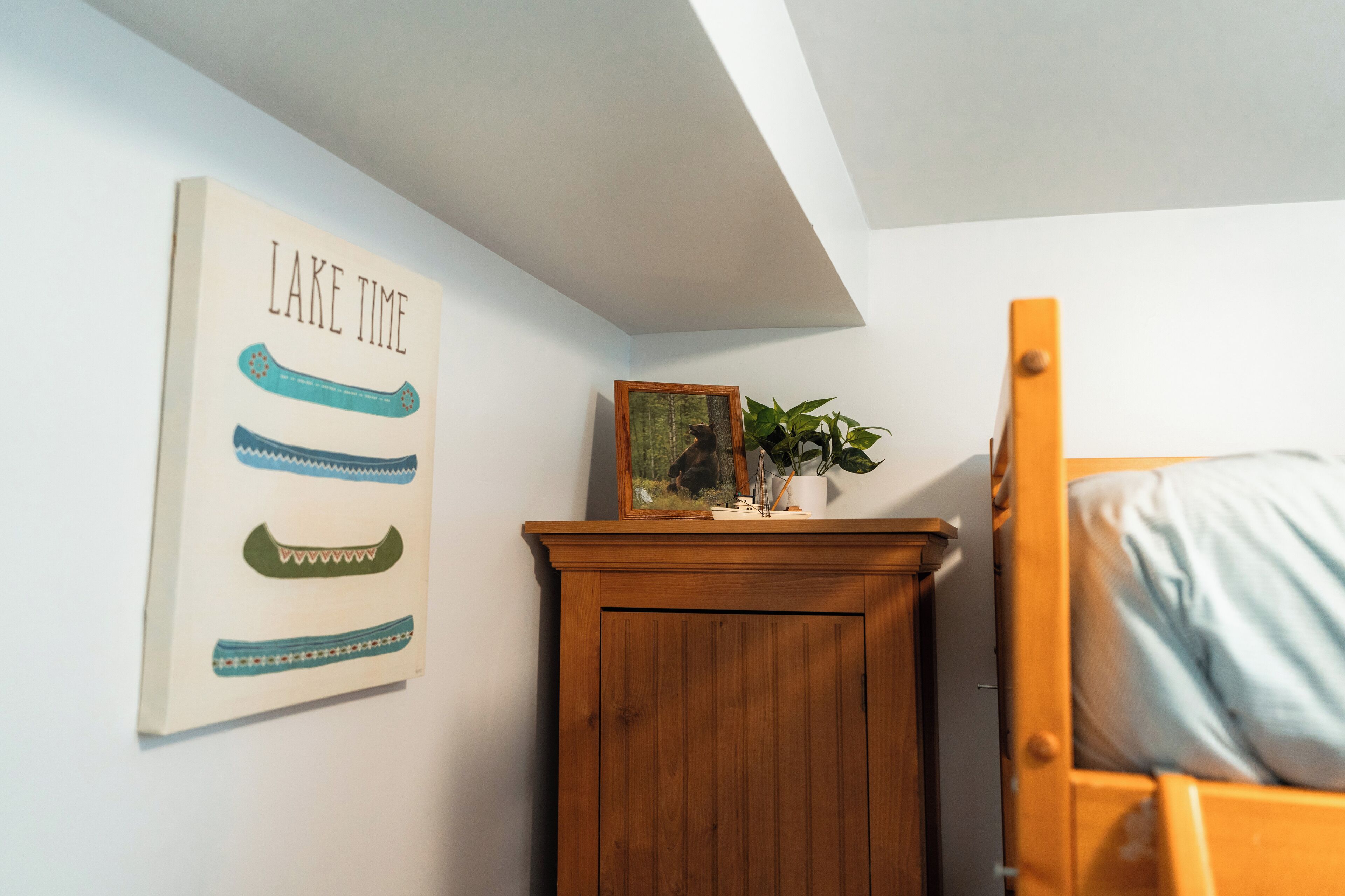 Un dormitorio con un armario de madera, una cama con almohada azul, un cuadro enmarcado y un cartel en la pared.