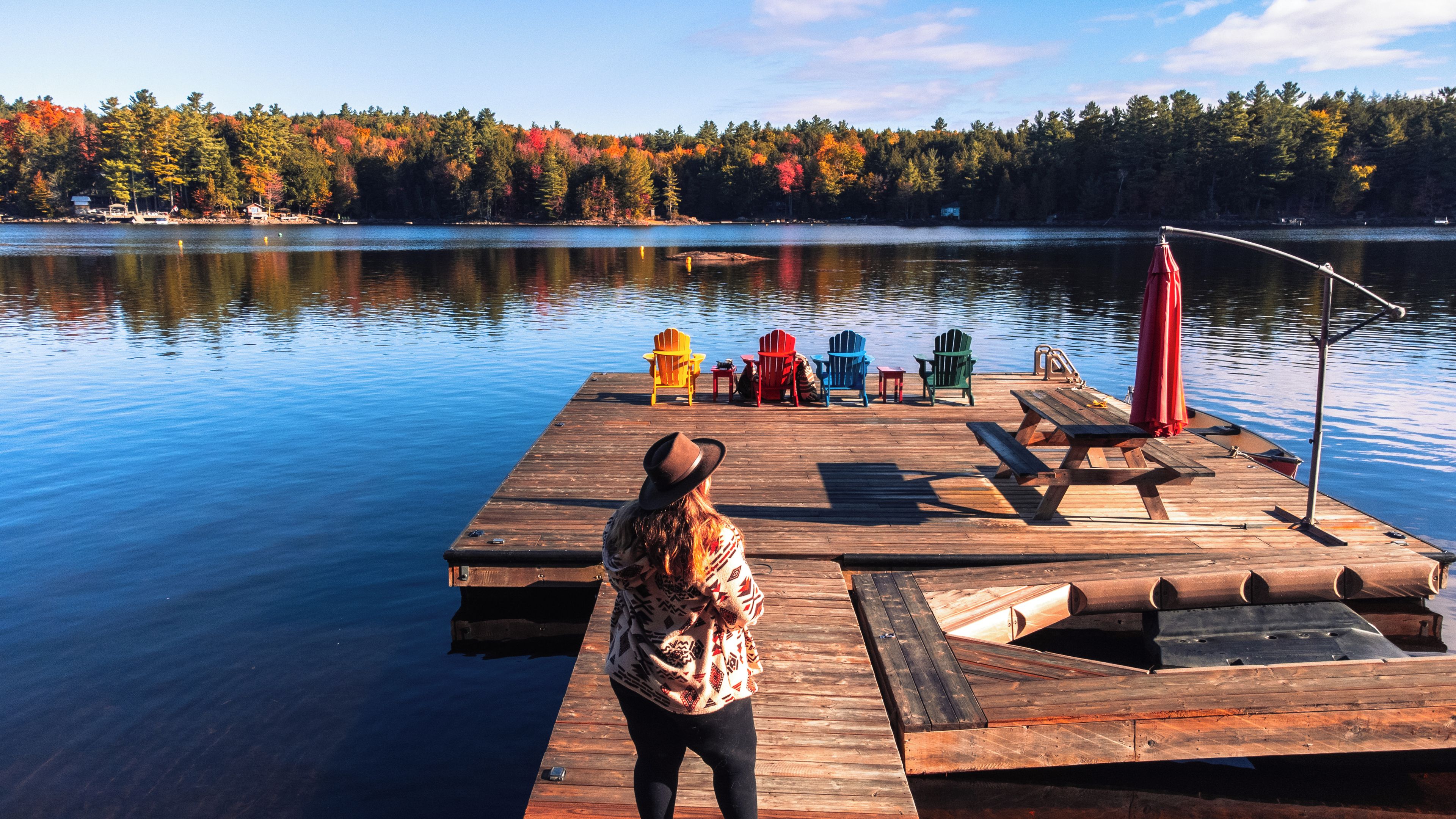 Une jetée en bois, bordée d’une rangée de chaises Adirondack aux couleurs vives et d’une table de pique-nique.