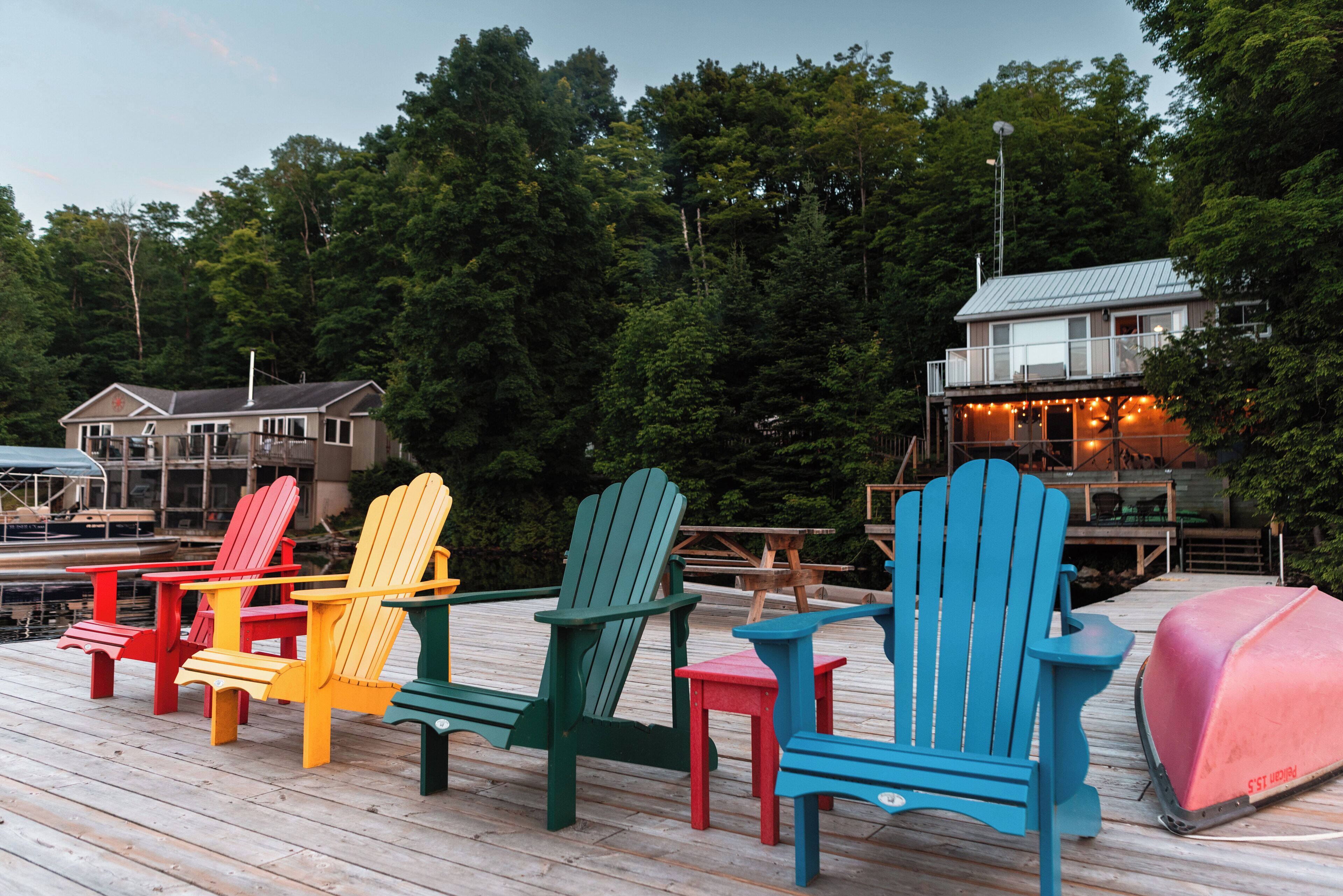 A wooden deck with colorful Adirondack chairs, a grill, and a house in the background.