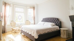 Une chambre à coucher avec un grand lit, deux fauteuils, une petite table et une cheminée.