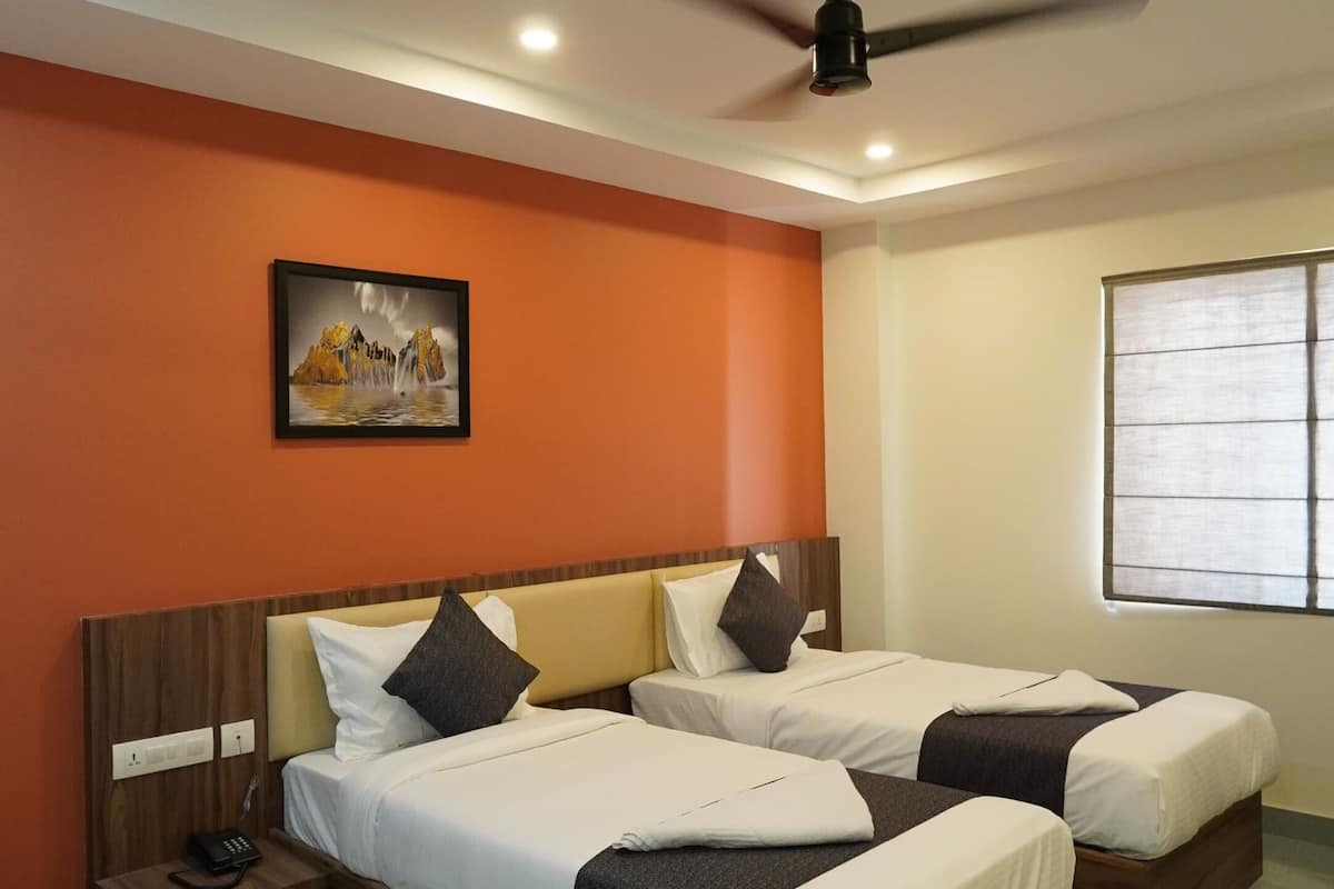 Une chambre d’hôtel avec deux lits, un ventilateur de plafond, un tableau au mur et une fenêtre avec des stores.