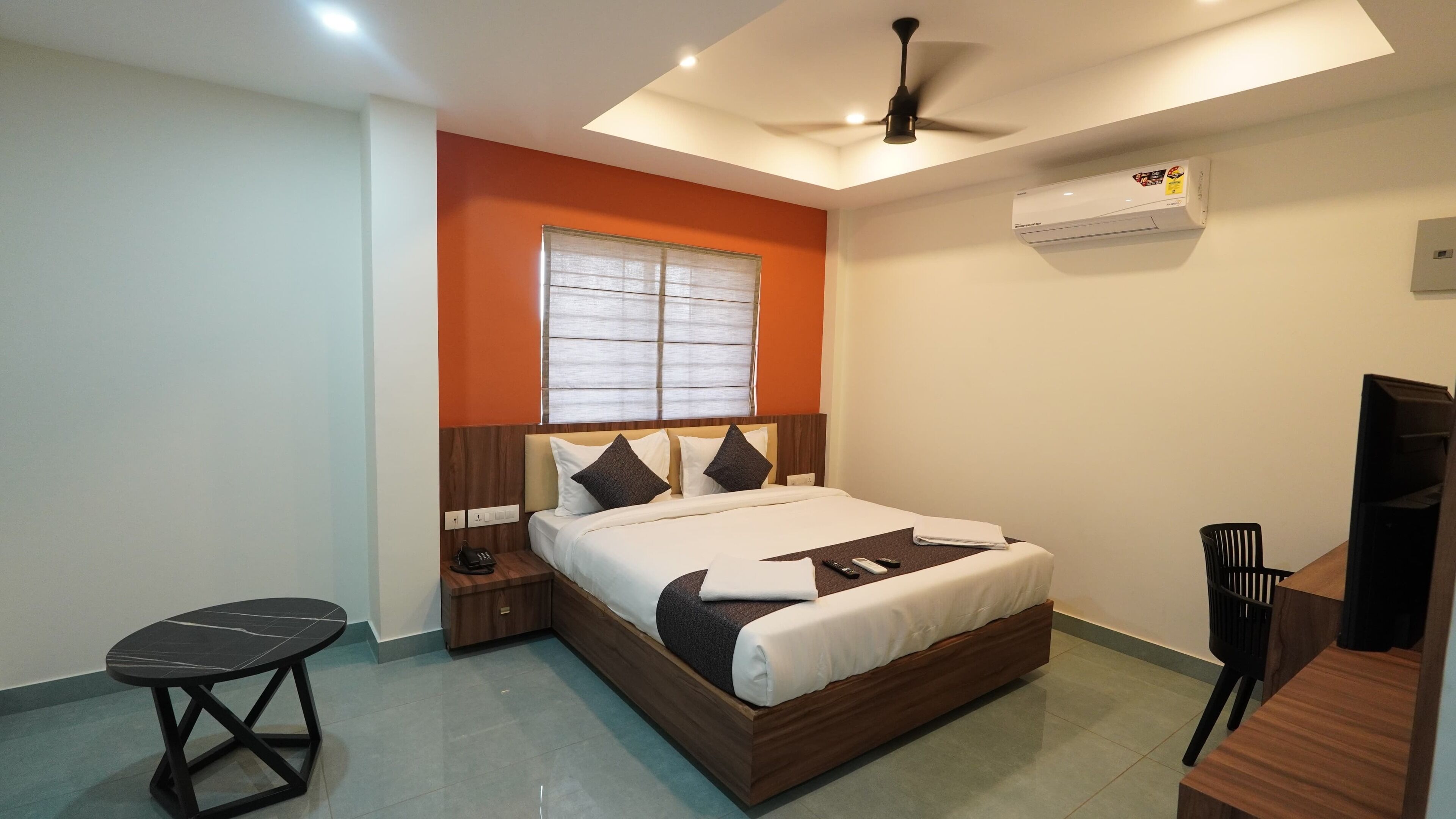 A modern hotel room with a wooden bed, a small table, a chair, and a ceiling fan.