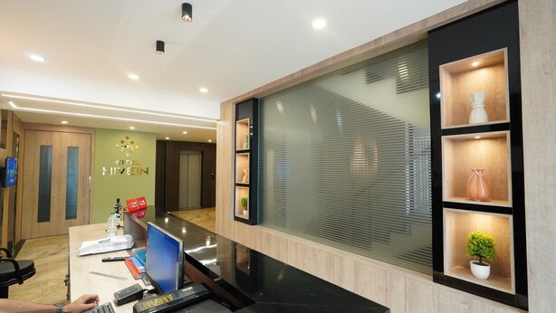 A hotel reception desk with a computer, a phone, and a digital display. There is a wall with a sign that reads "HOTEL HIVEIN". - Hotel Hive Inn (Kozhikode)