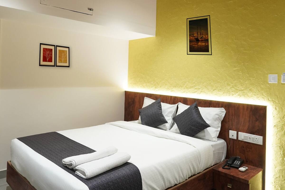 Une chambre moderne avec un plafond en bois, un lit recouvert de draps blancs, une table de chevet et un téléphone fixé au mur.