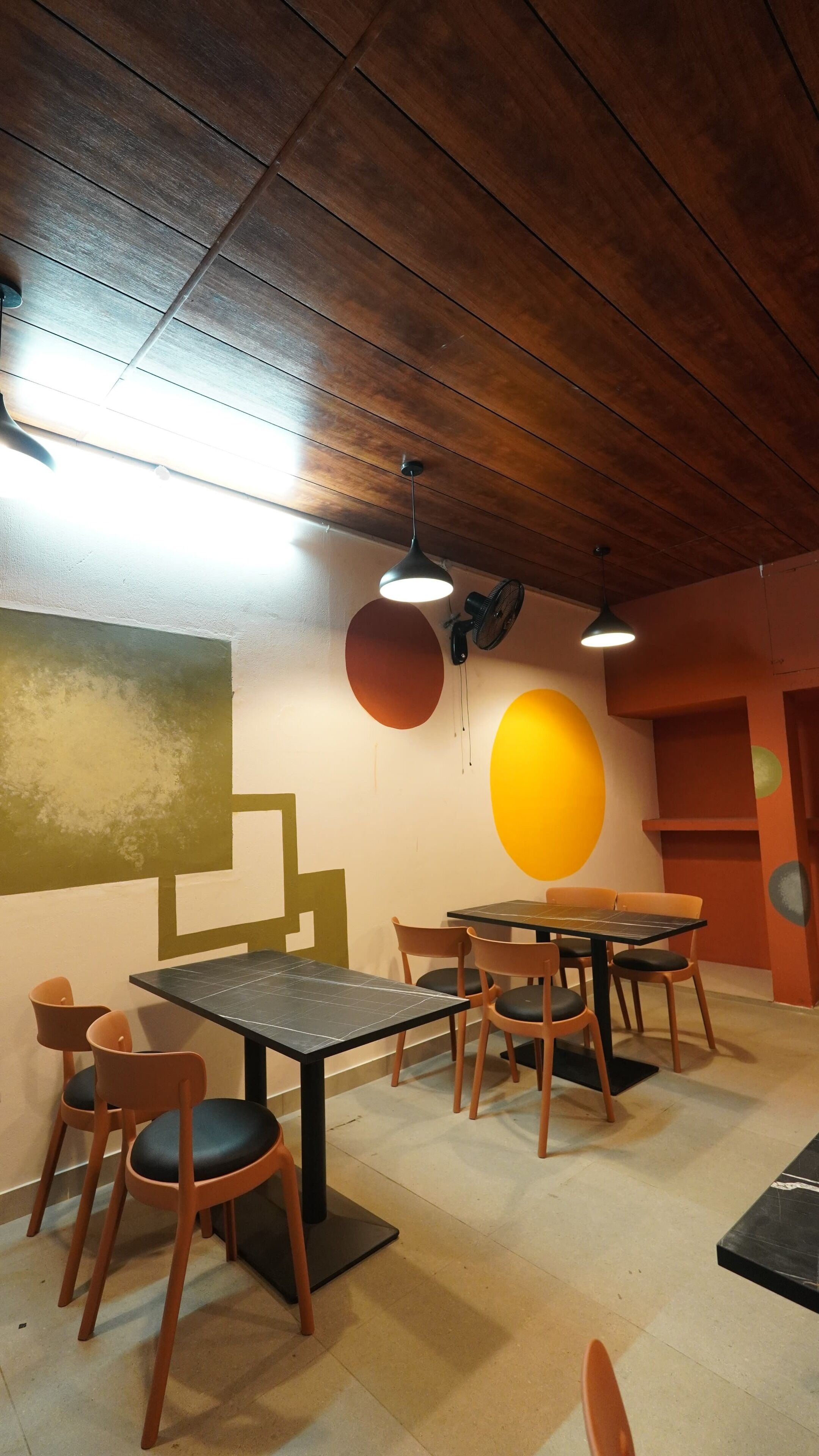 Un comedor con mesas y sillas de madera, un ventilador y un ventilador de techo.