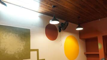 Un comedor con mesas y sillas de madera, un ventilador y un ventilador de techo.