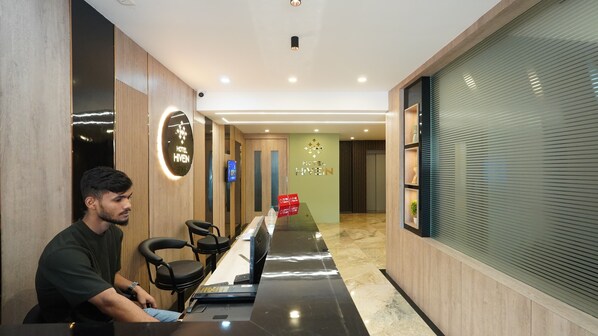 A hotel reception area with a reception desk, chairs, and a digital screen.