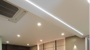 A spacious room with a large blue and beige sofa, a ceiling vent, recessed lighting, and a tiled floor. - Hotel Hive Inn (Kozhikode)