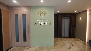 A hotel reception area with a modern design, featuring a reception desk, a wall-mounted sign, and a door with a vertical handle. - Hotel Hive Inn (Kozhikode)
