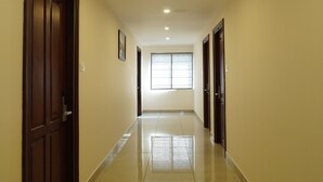 A long, well-lit hallway with a tiled floor, wooden doors, and a window at the end. - Hotel Hive Inn (Kozhikode)