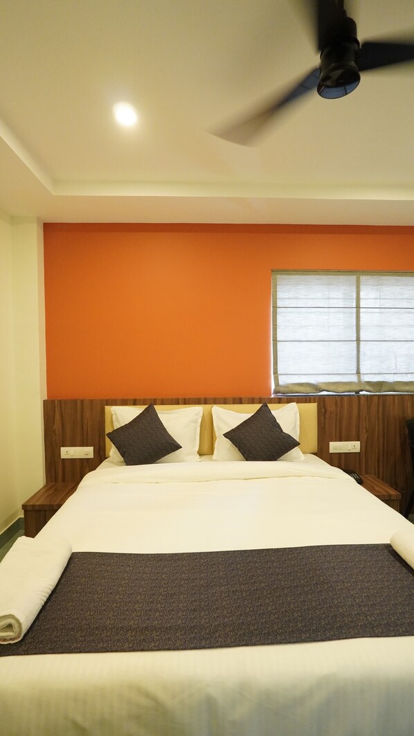 A hotel room with a bed, a ceiling fan, a window with blinds, and wooden headboards.