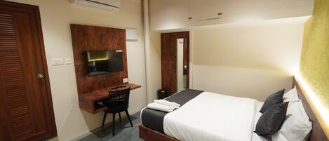 A hotel room with a wooden bed, a desk with a chair, a flat-screen TV, and a mirror.