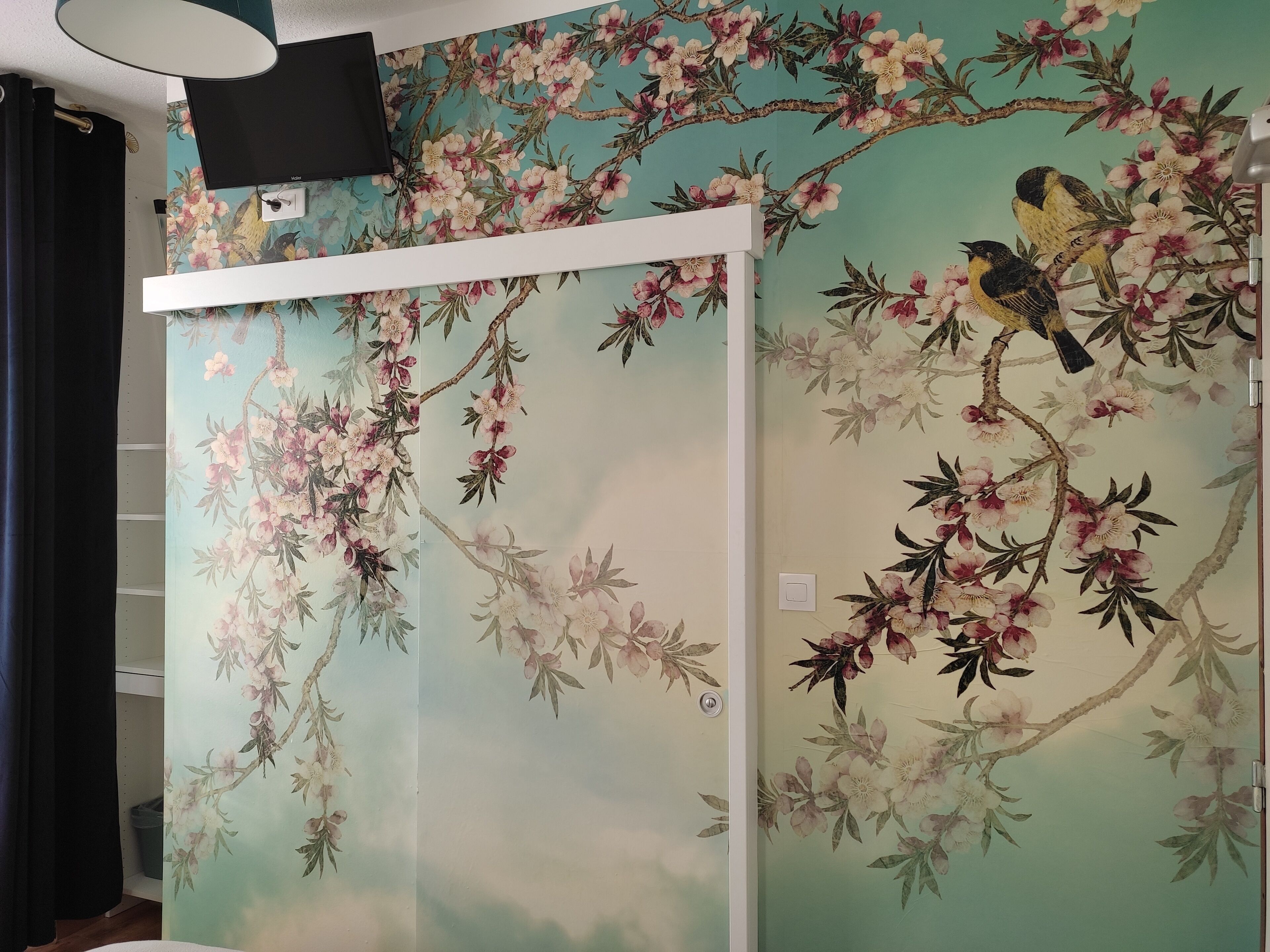 Een kamer met een wand versierd met bloemenbehang met vogels en takken.