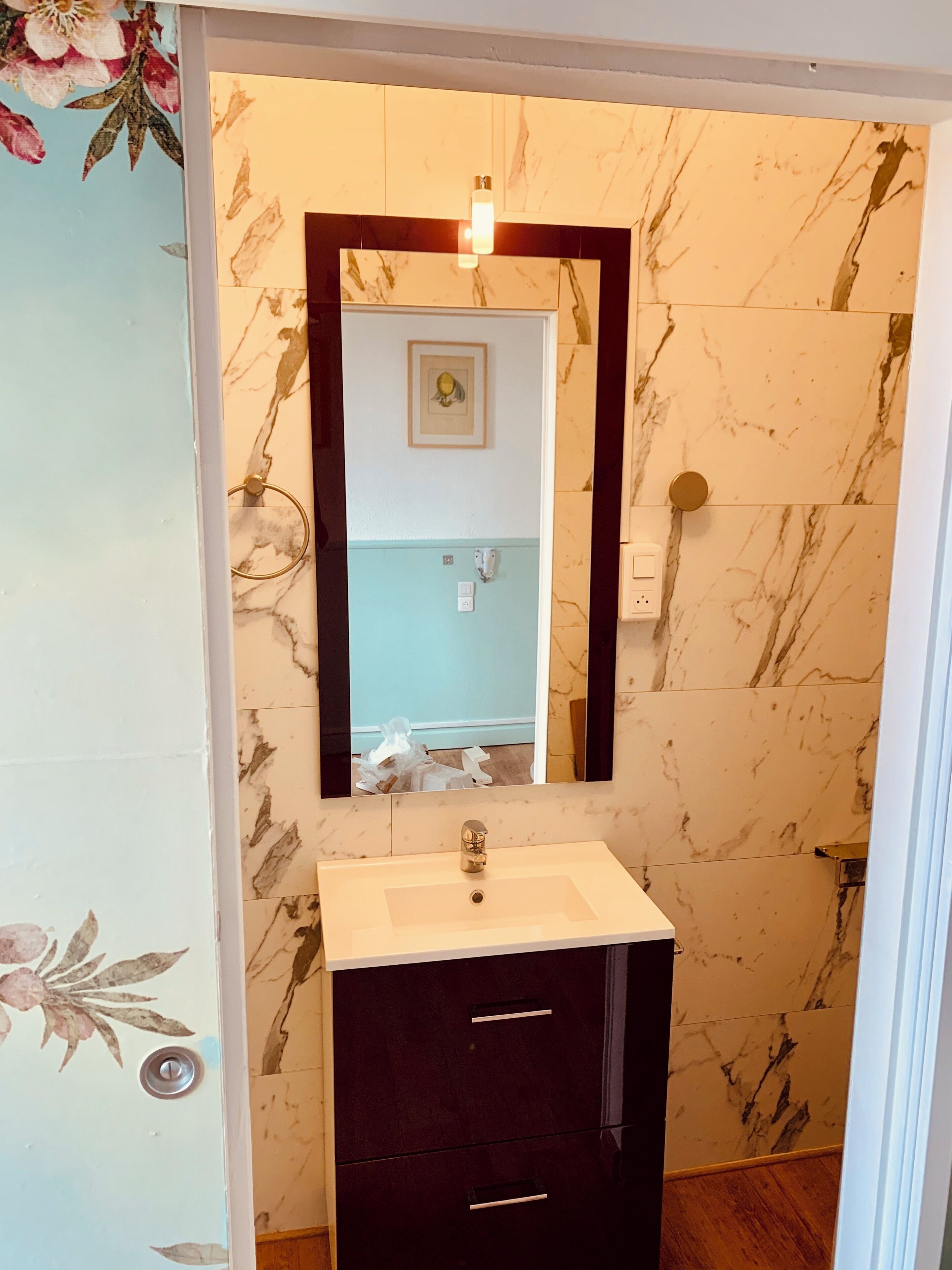 A bathroom with a marble wall, a white sink, a dark cabinet, and a mirror with a light fixture above it.