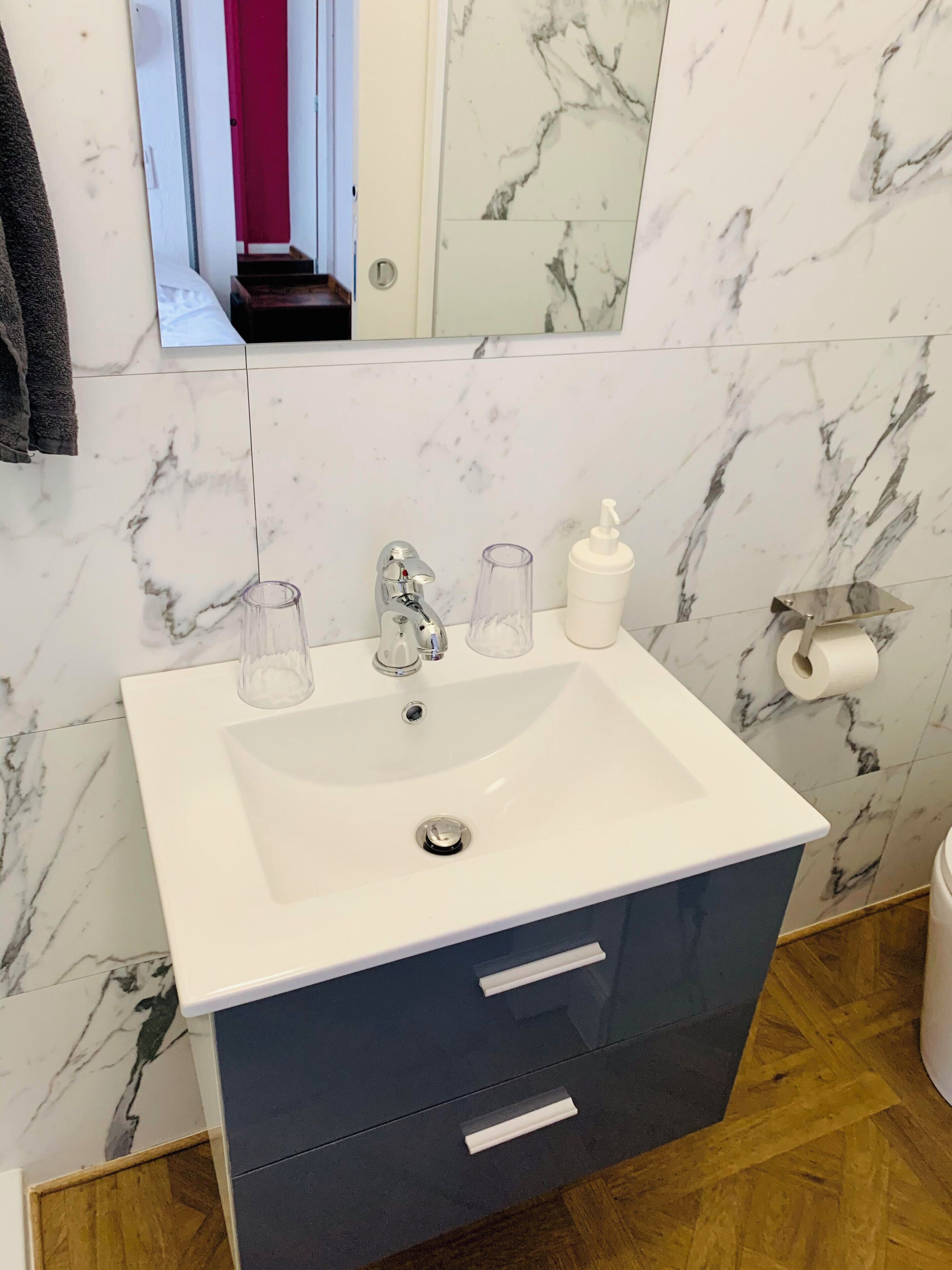 A bathroom with a white sink, two drawers, a mirror, and a marble-patterned wall.