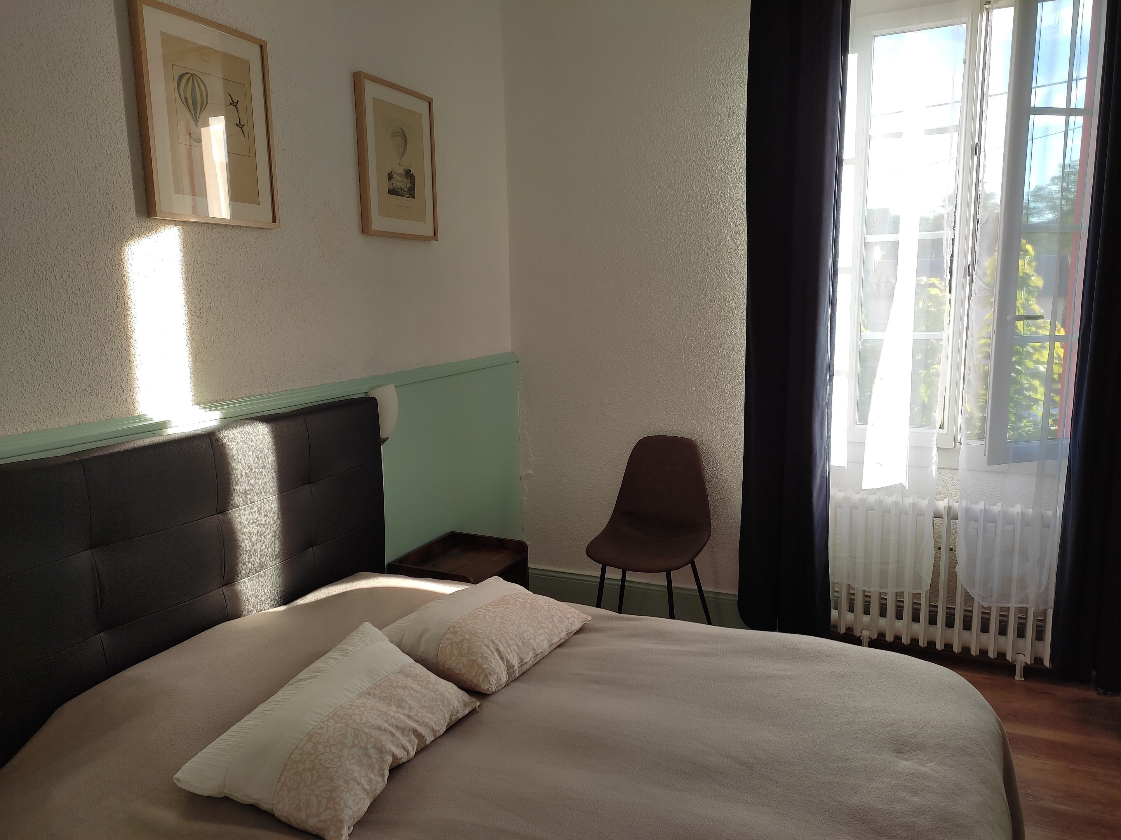 Un dormitorio con una cama, una silla y dos cuadros en la pared.