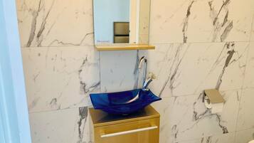 Un baño con pared de mármol, un mueble dorado, un lavamanos azul y un dispensador de papel higiénico.