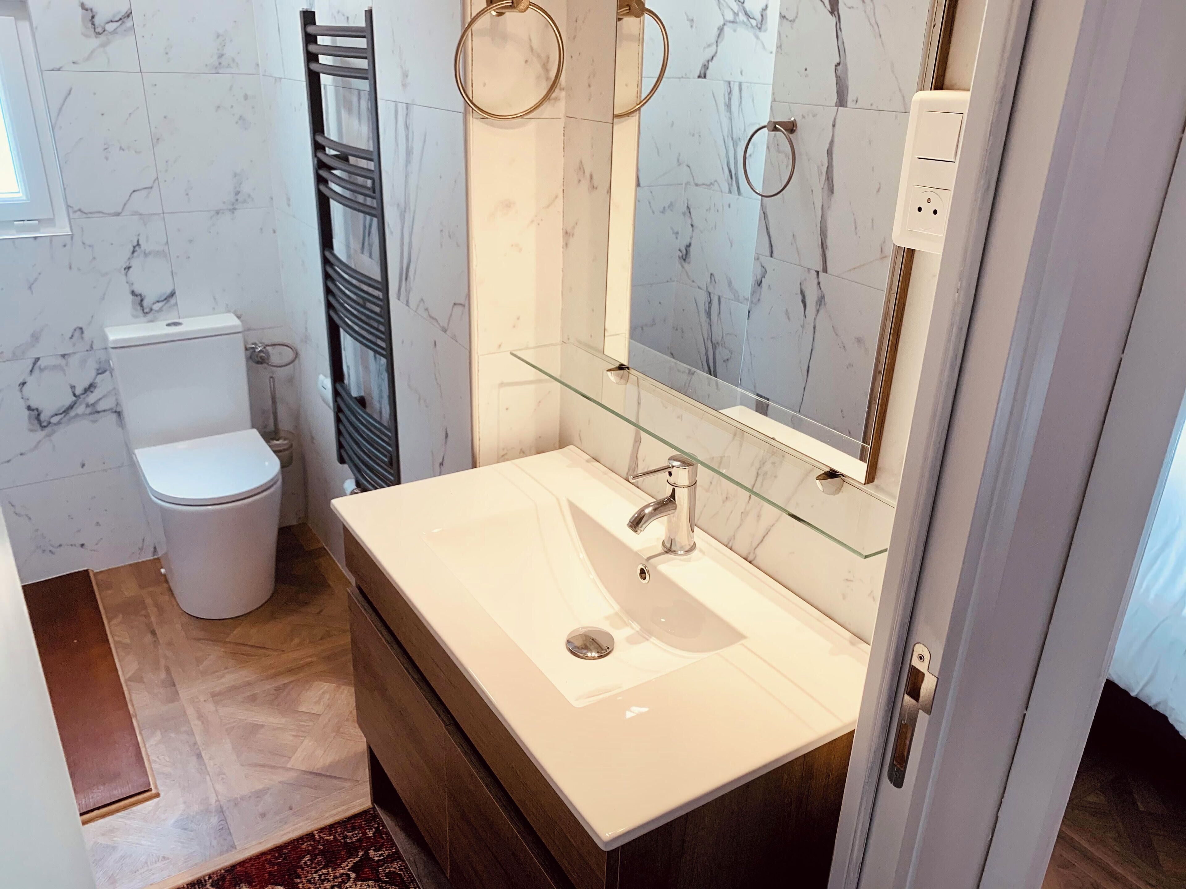A modern bathroom with a white toilet, a glass shelf above the sink, and a marble-tiled wall.