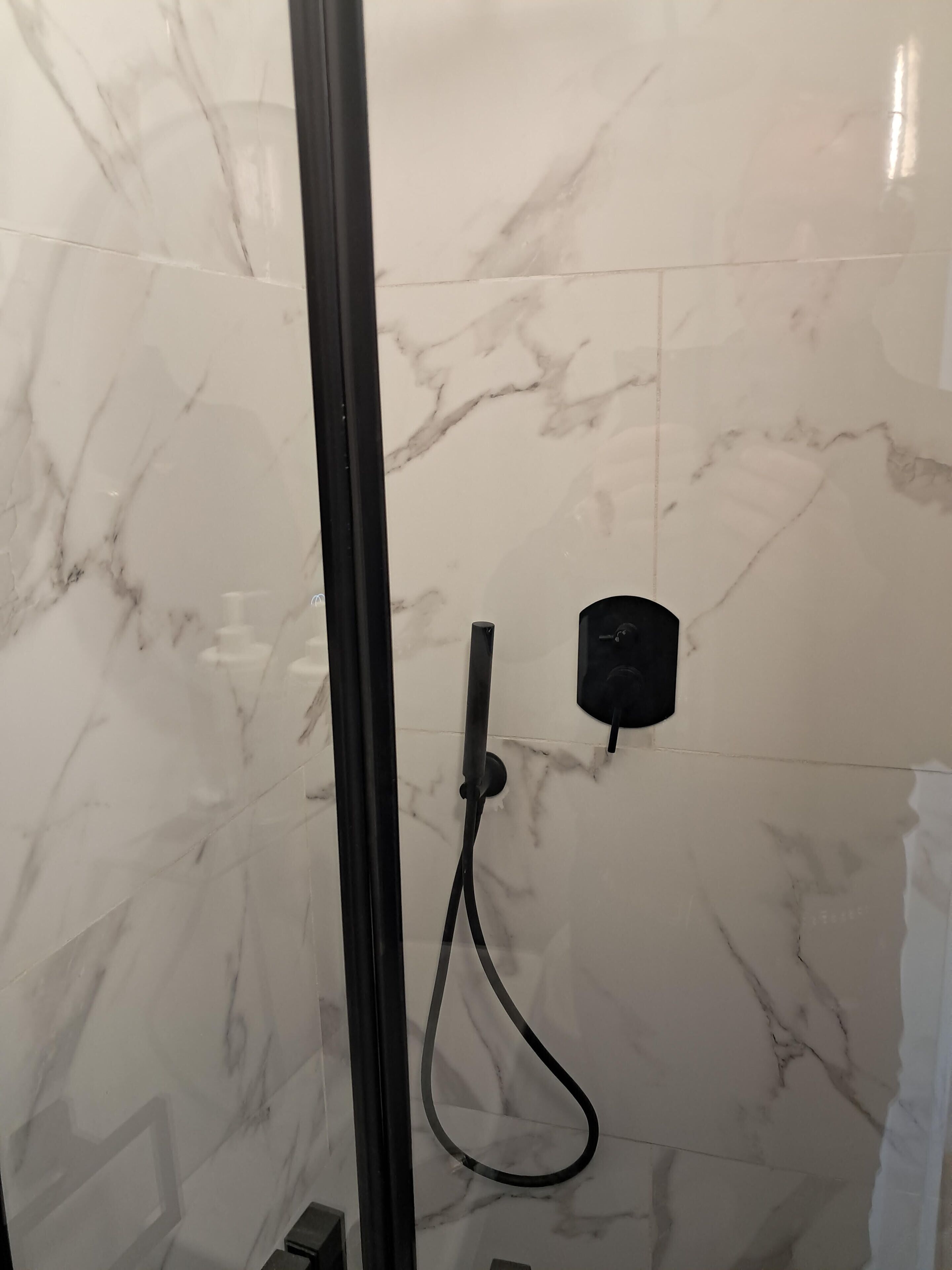 A bathroom with a glass shower enclosure, marble walls, and a black handheld showerhead.
