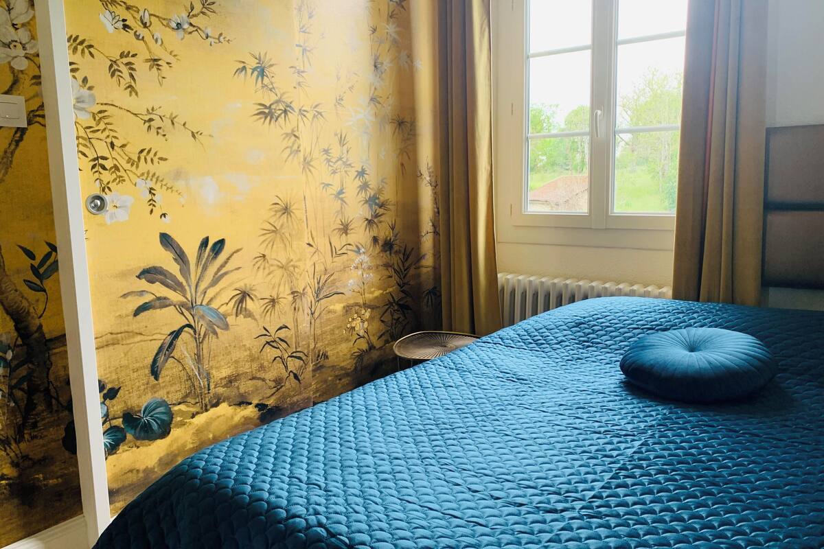 Een kamer met een bed, een radiator, een raam met gordijnen en een wand met bloemenbehang.