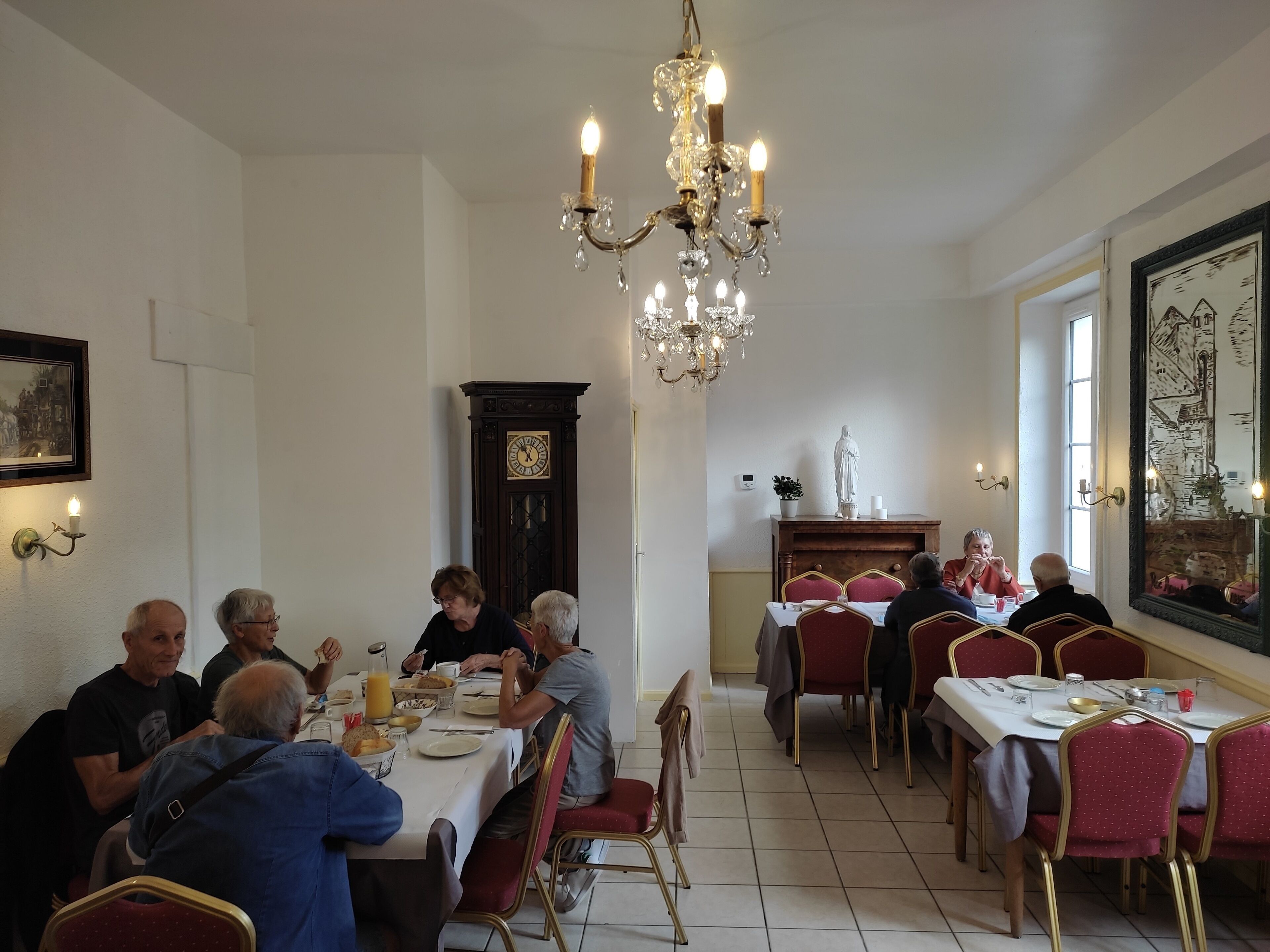 Un comedor con una araña, un reloj y una estatua sobre la chimenea.