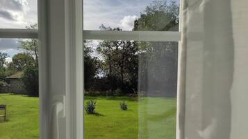 Uitzicht door een raam met een witte lijst, waarop een gazon, een fiets en een stenen gebouw in de verte te zien zijn.